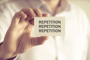 Person holding a card with 'REPETITION' written three times.